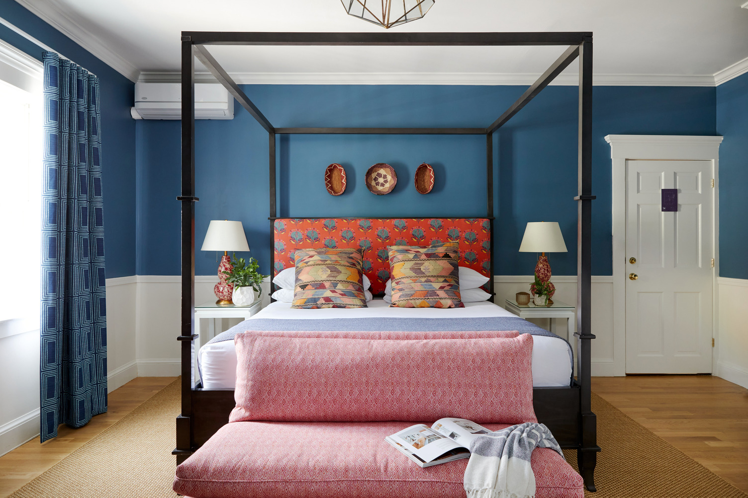 Queen canopy bed with a comfy bench with pink cushions at the foot of the bed
