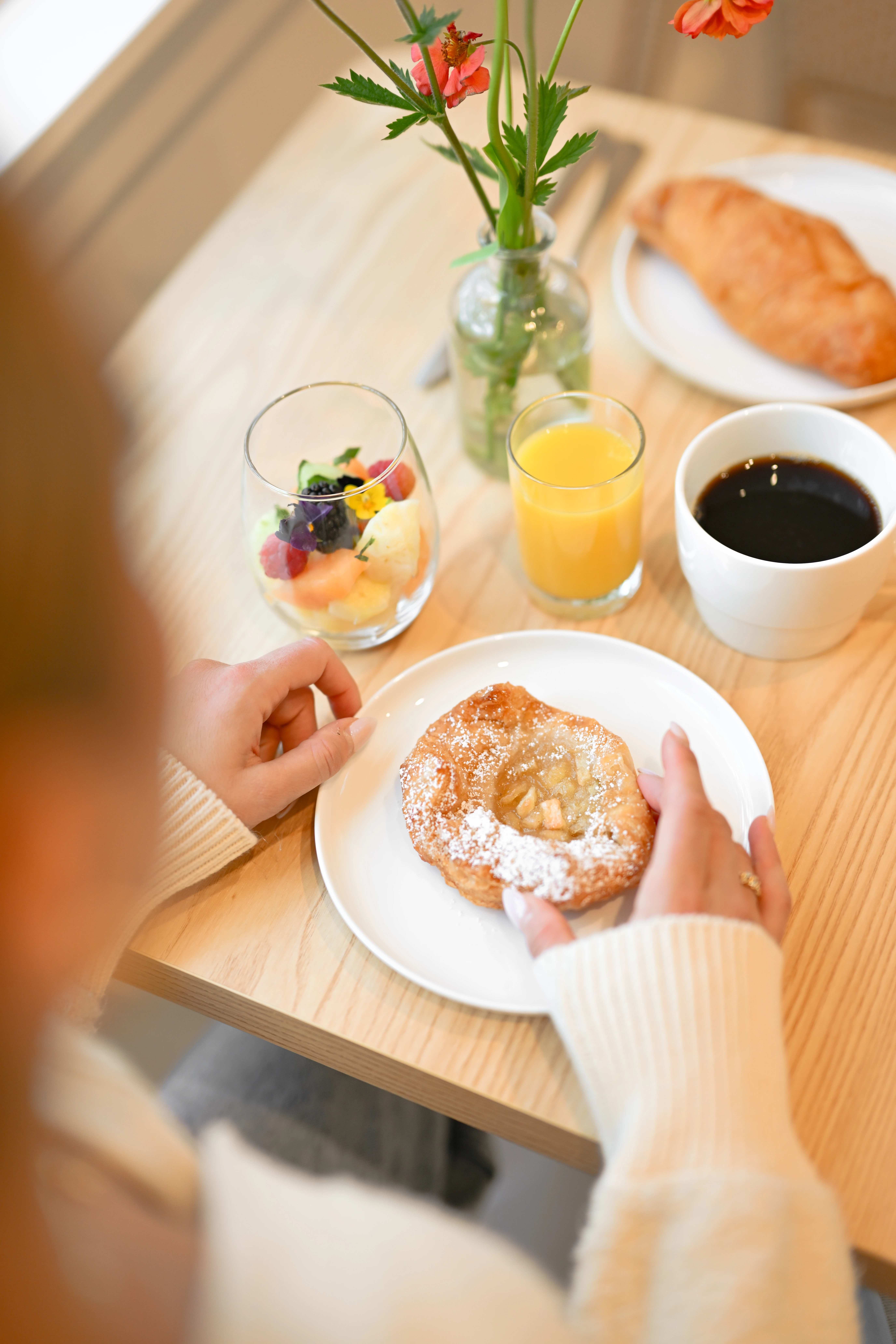 Person enjoying their breakfast of a pastry, cup of fruit, orange juice and coffee