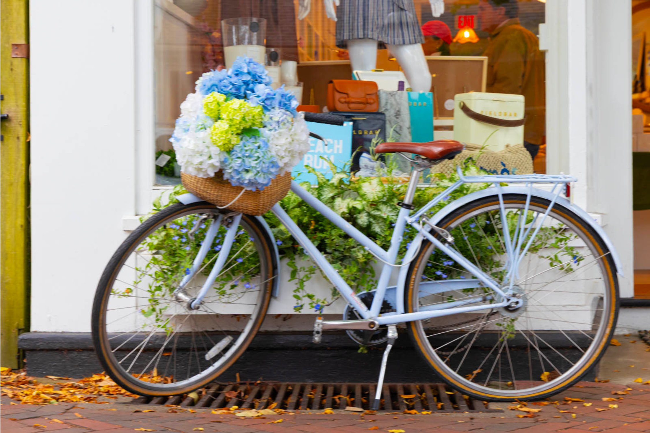 A bike with a basket full of hydrangeas in front of a storefront in downtown Nantucket