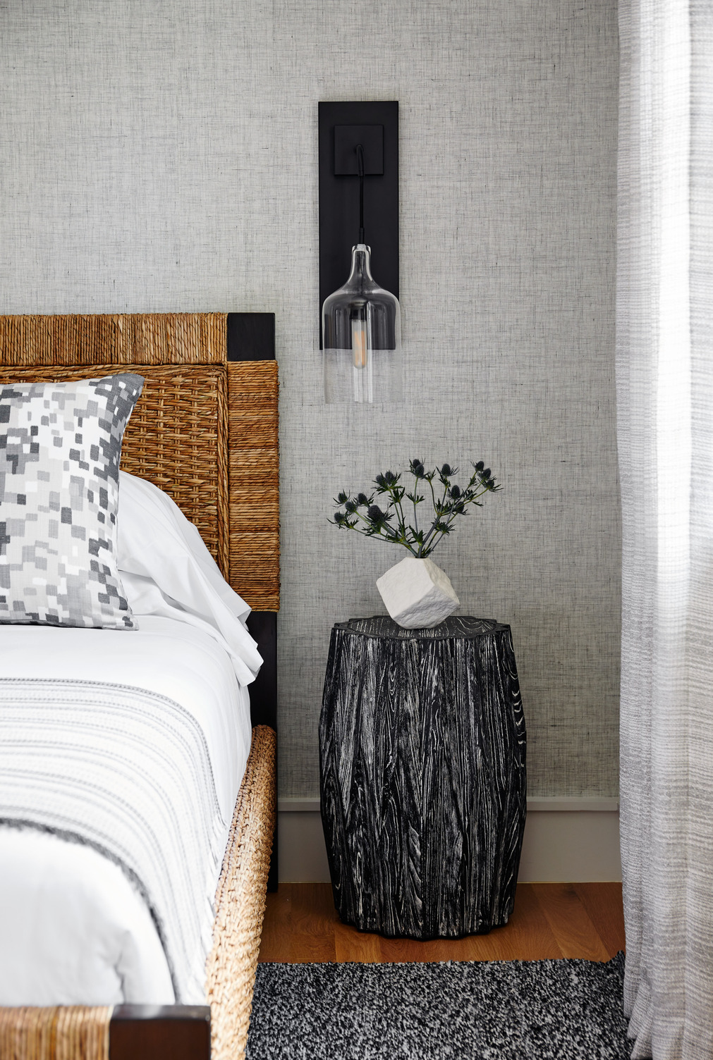 Bedside table with a plant on top and a sconce above it